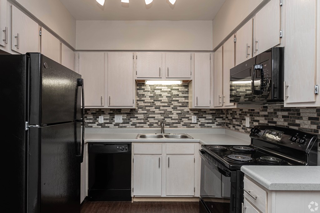 A black refrigerator is on the left in a kitchen with white cabinets.
