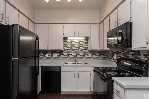 A black refrigerator is on the left in a kitchen with white cabinets.