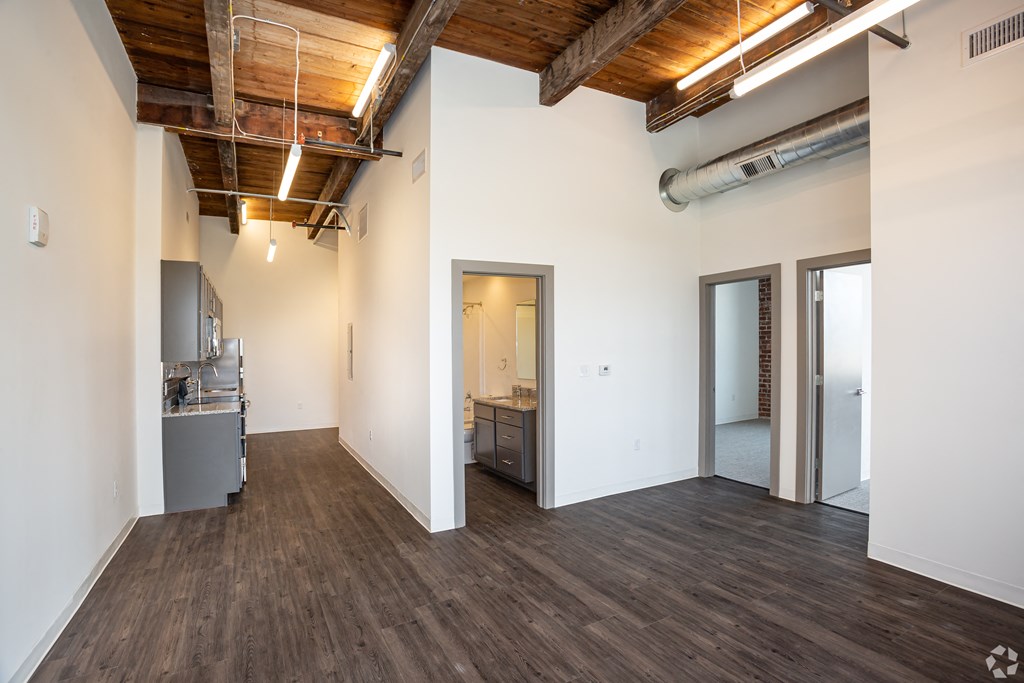 a living room with white walls and wood floors and a kitchen