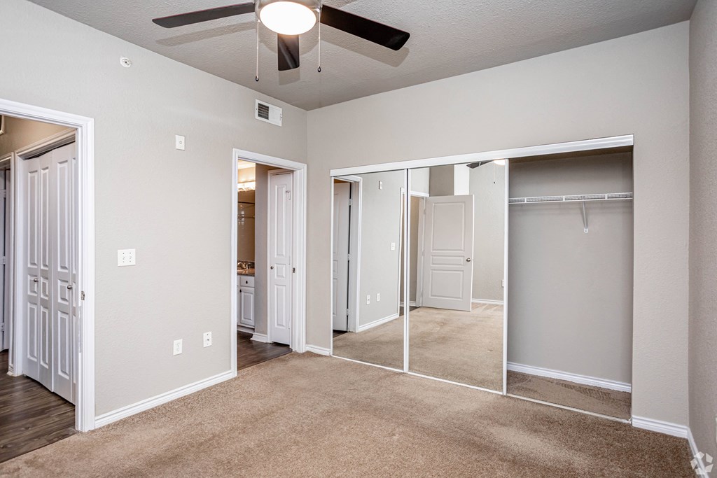 an empty bedroom with mirrored closet doors and a ceiling fan