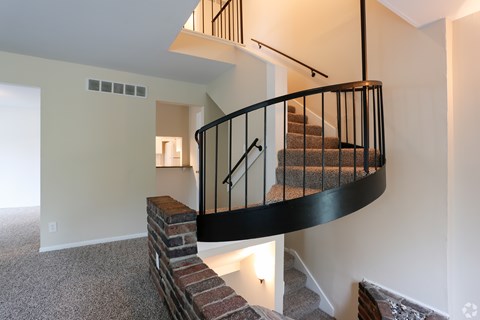 A staircase with a black railing and a brick base leads to a second floor.