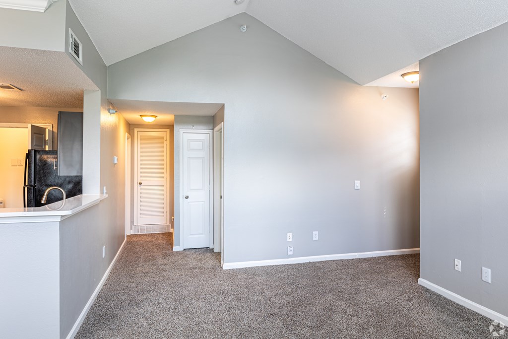 A spacious living room with a kitchen area to the left and a doorway leading to another room.
