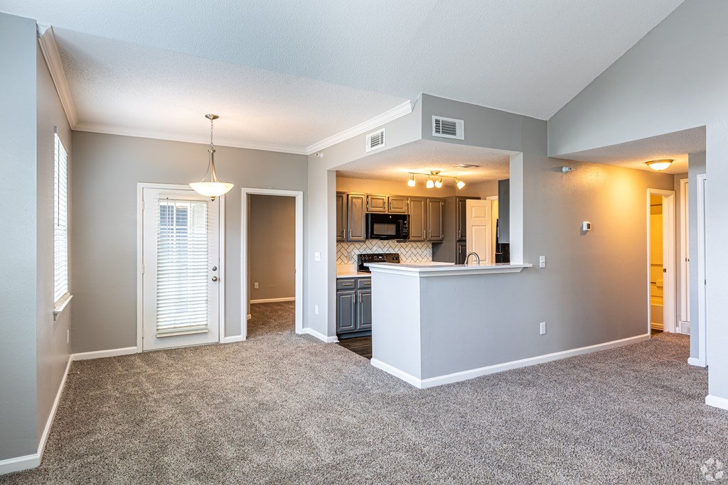 A spacious living room with a kitchen area in the background.
