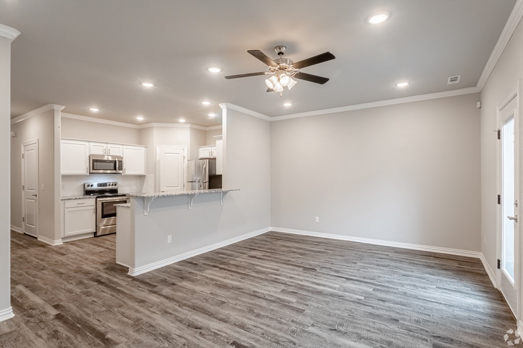 a living room with a ceiling fan and a kitchen in the background