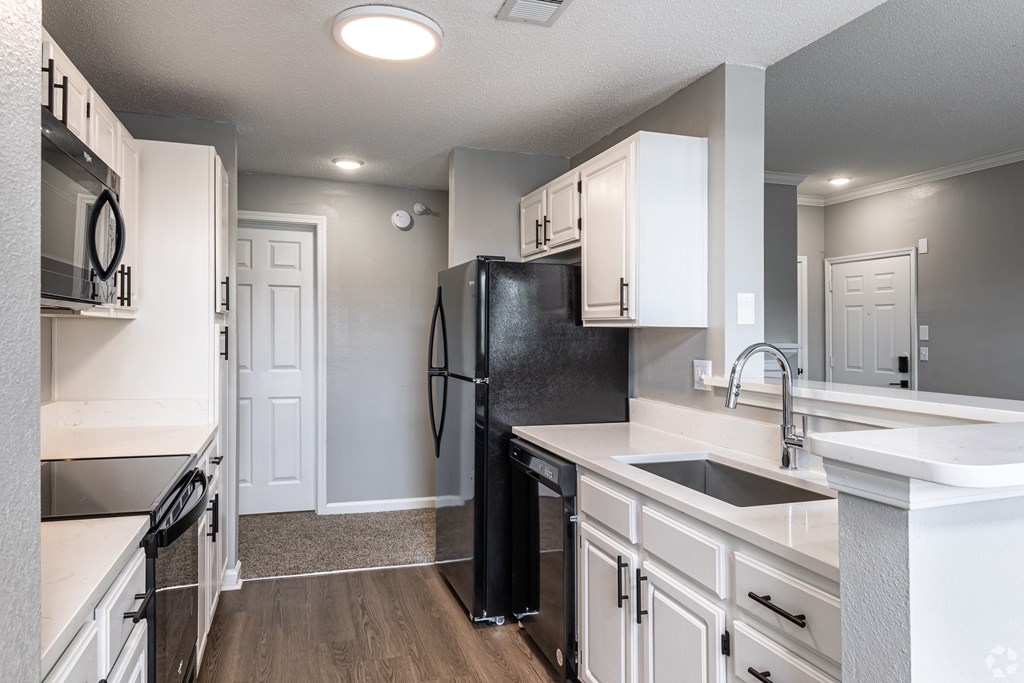 A black refrigerator in a kitchen with white cabinets.