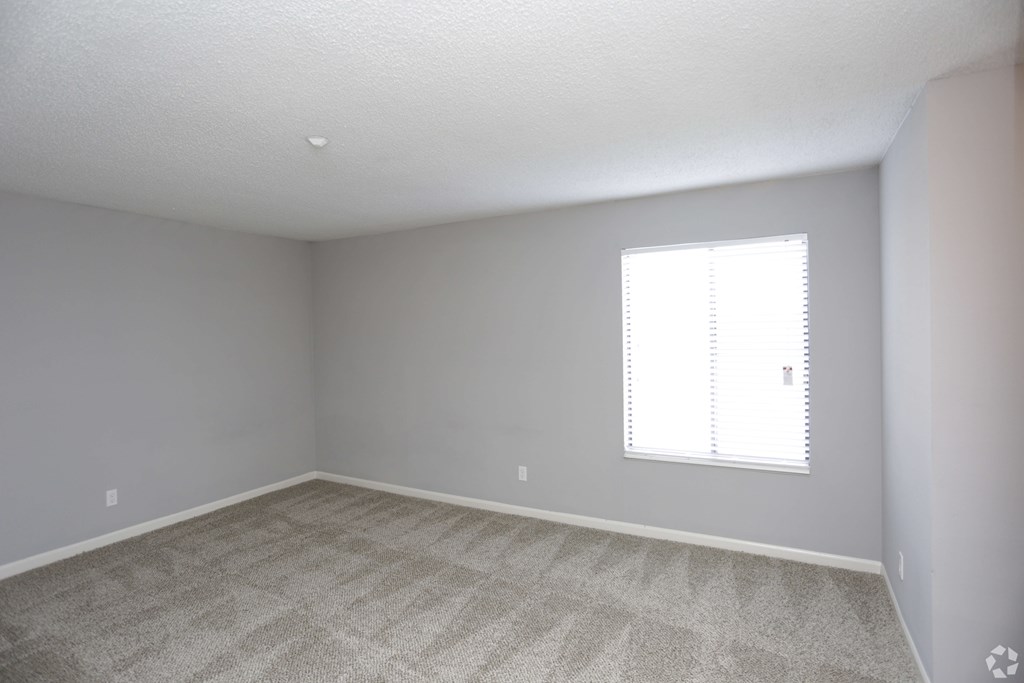 A room with a carpeted floor and a window with blinds.