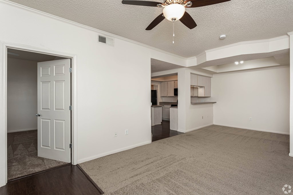 A spacious living room with a ceiling fan and carpeted floor.