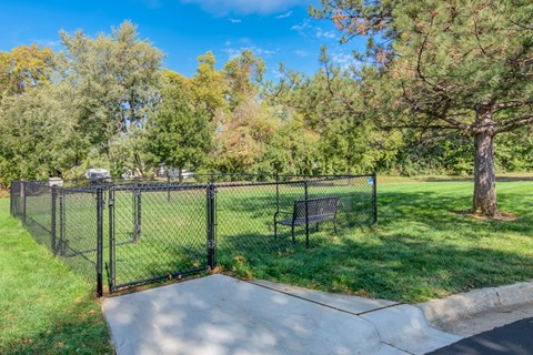 A black fence surrounds a park bench in the middle of a grassy area.