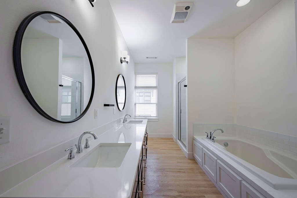 A white bathroom with a round mirror and a white sink.