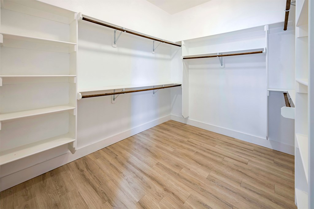 A walk-in closet with white shelves and wooden floors.