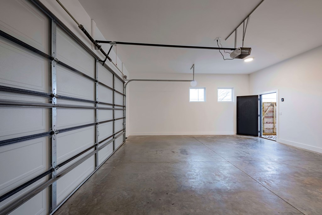 A spacious garage with a concrete floor and a black door at the far end.