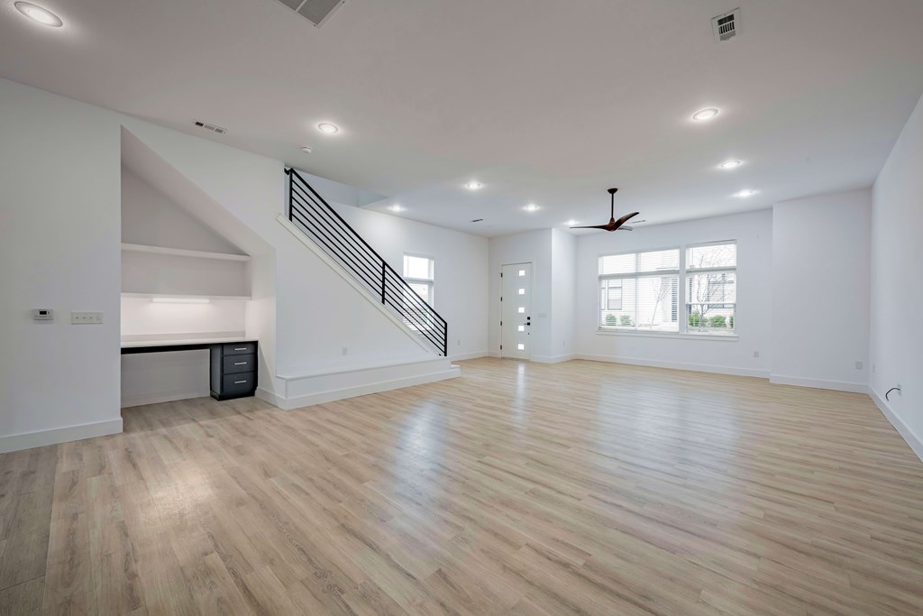A spacious room with wooden flooring and a staircase.