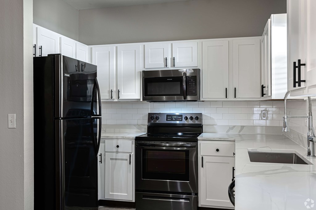 A black refrigerator stands next to a black stove in a kitchen with white cabinets.