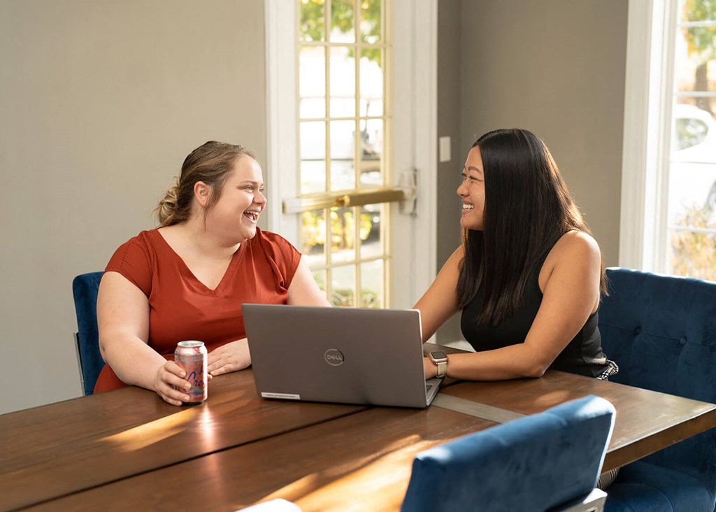 two women sitting at a table with a laptop