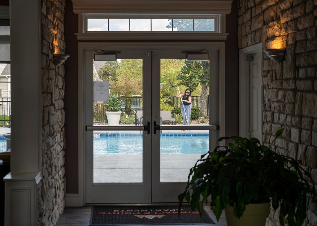 A woman is standing in the doorway of a house with a pool in the backyard.
