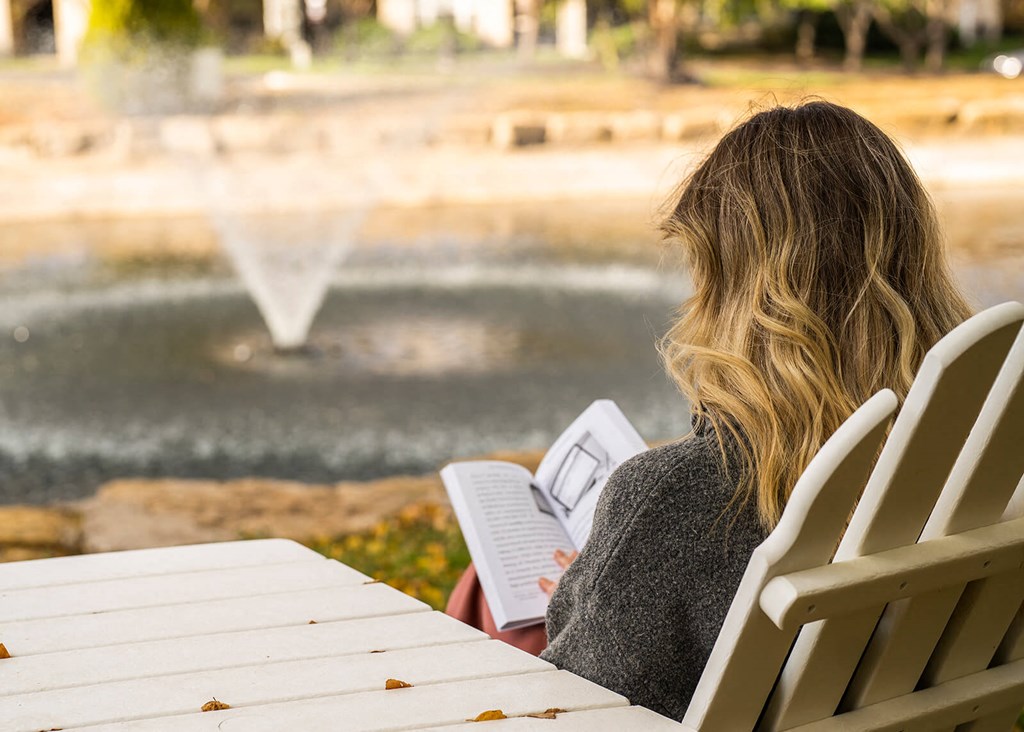 a woman sitting in a chair reading a book in front of a fountain
