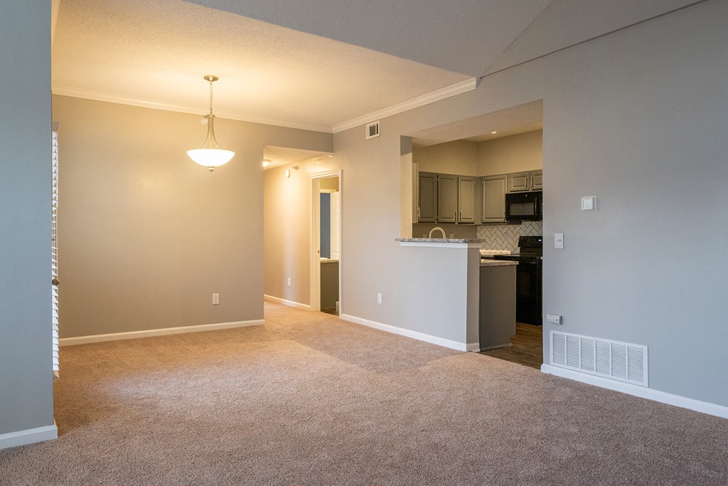 an empty living room with a kitchen in the background