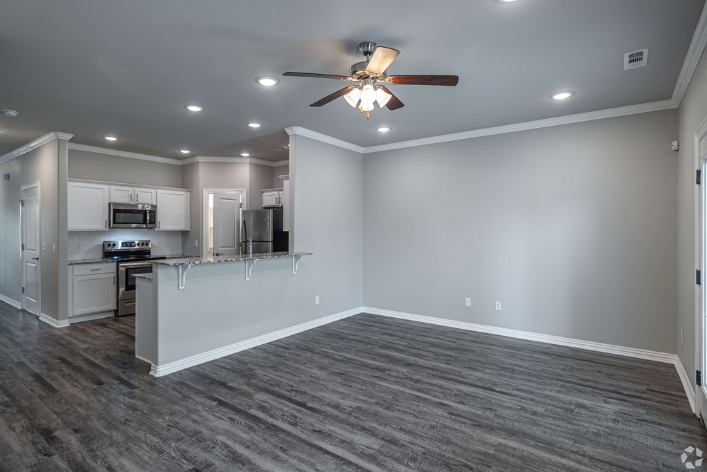 A spacious kitchen and living room with a ceiling fan and lighting.