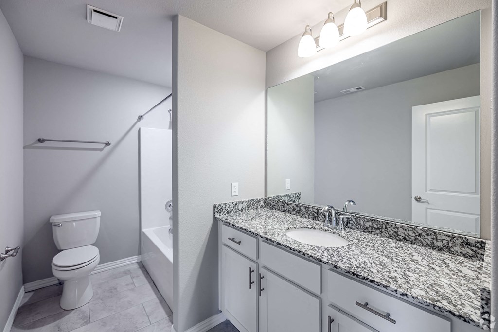 A bathroom with a granite counter top and white cabinets.