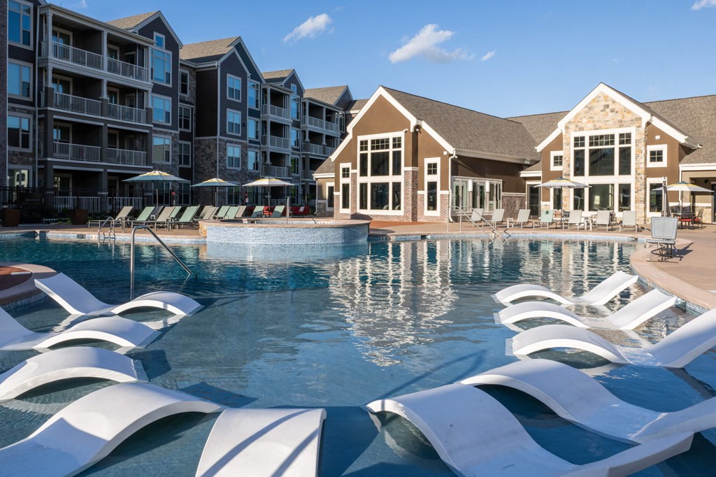a large pool with white chairs in front of an apartment building