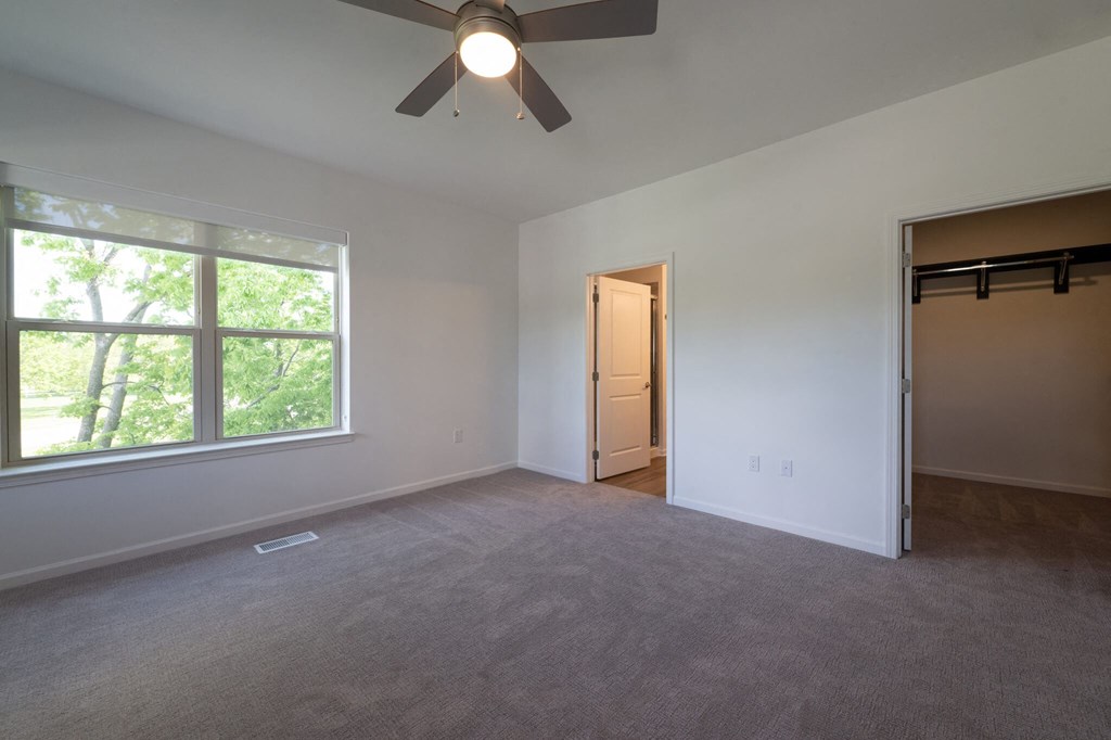an empty living room with a large window and a ceiling fan