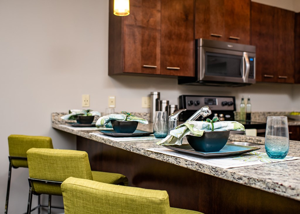 A kitchen with a counter, chairs, and a microwave.