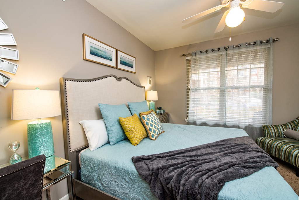 A bedroom with a bed, a ceiling fan, and a window with blinds.