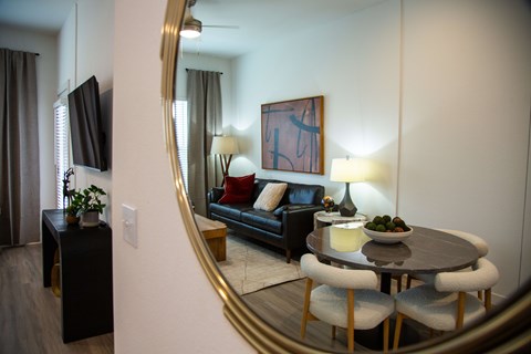 A living room with a black couch, a round table with four chairs, a television, and a large mirror.