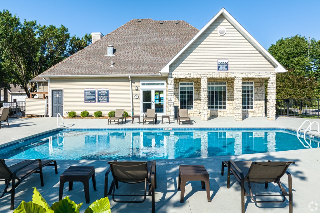 A poolside lounge area with chairs and tables is in front of a house.