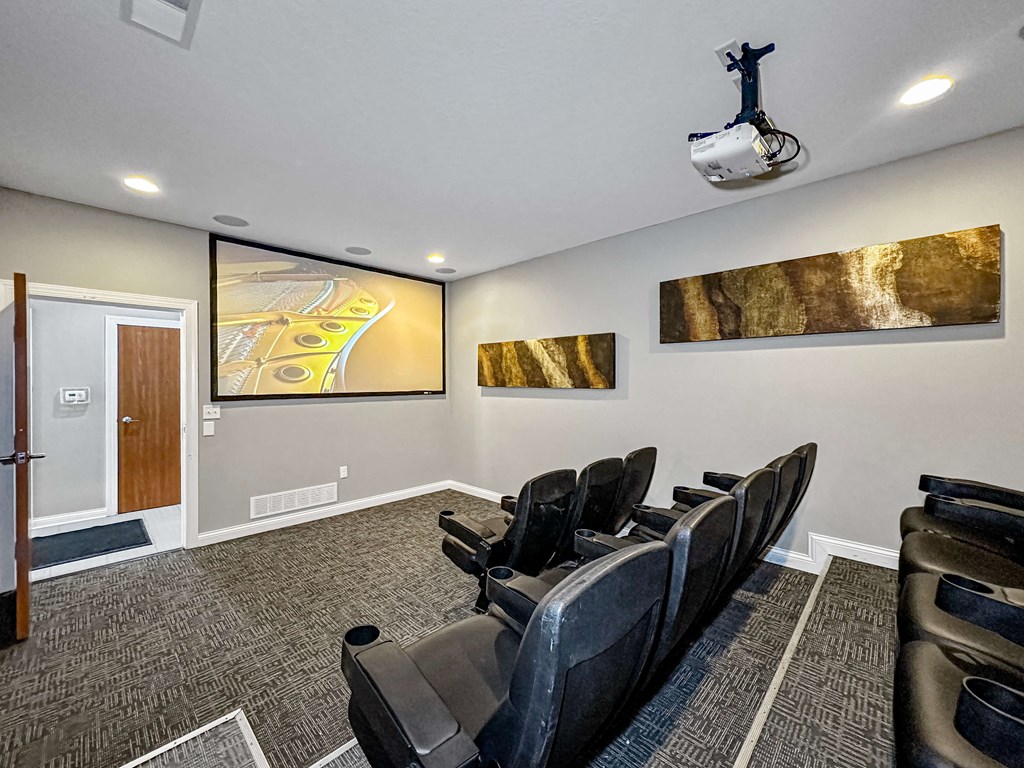 A room with a row of black chairs and a projector screen.