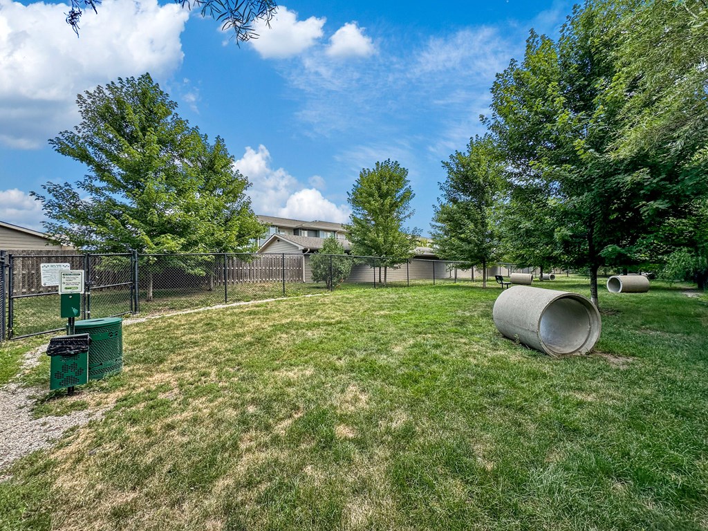 A grassy field with trees and a fence in the background.