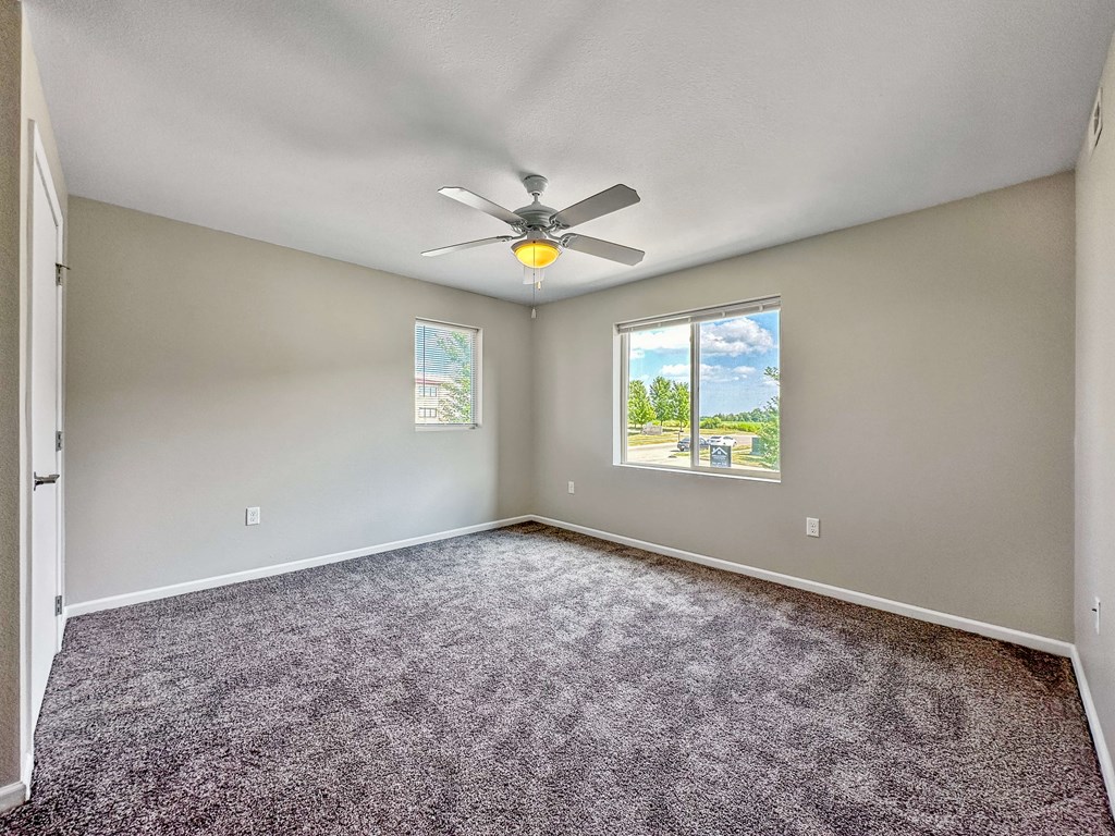A room with a ceiling fan and two windows.
