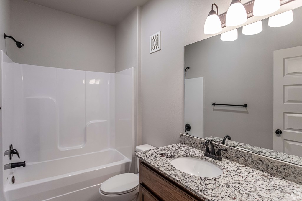 the retreat guest bathroom with granite counter top and white tub and shower