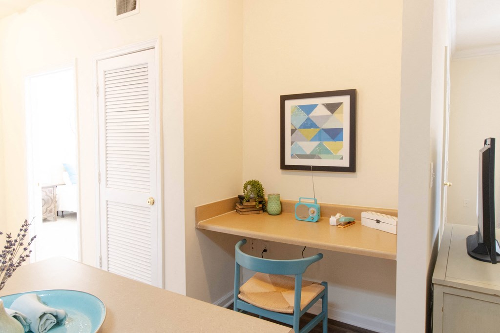 A blue chair sits in front of a desk with a plant on it. at The Crest at Sugarloaf, Lawrenceville, Georgia