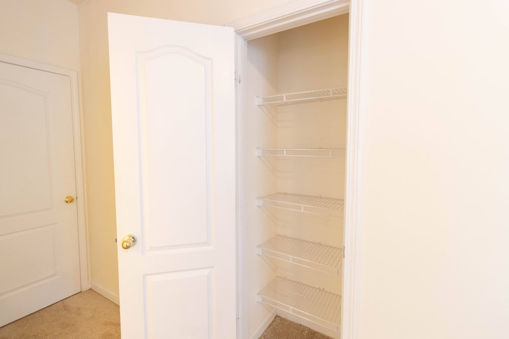 A white door is open to reveal a white pantry with empty shelves. at The Crest at Sugarloaf, Lawrenceville, Georgia
