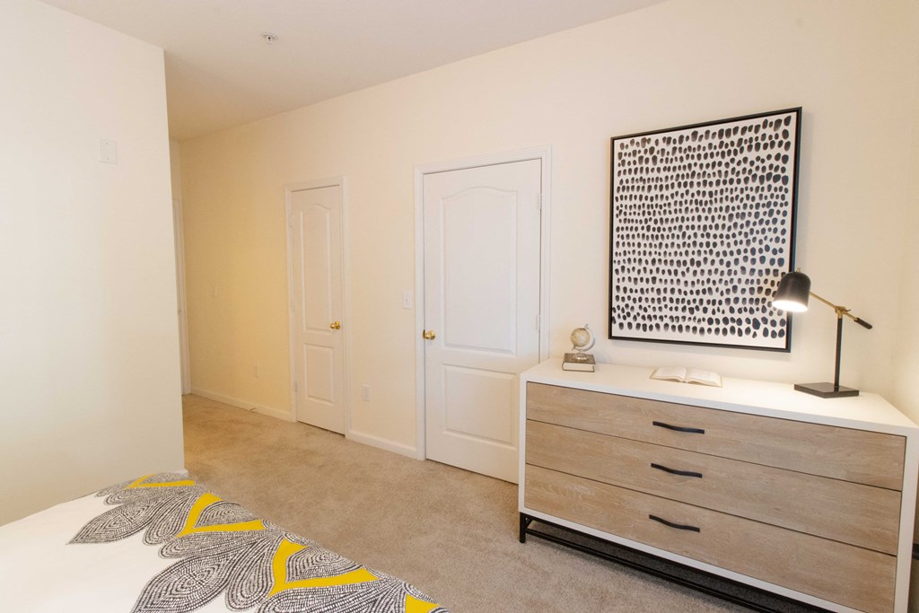 A bedroom with a bed, dresser, and a wall hanging picture. at The Crest at Sugarloaf, Lawrenceville, GA