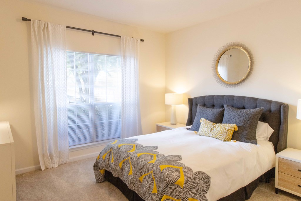 A bedroom with a large bed and a round mirror on the wall. at The Crest at Sugarloaf, Lawrenceville, GA, 30044