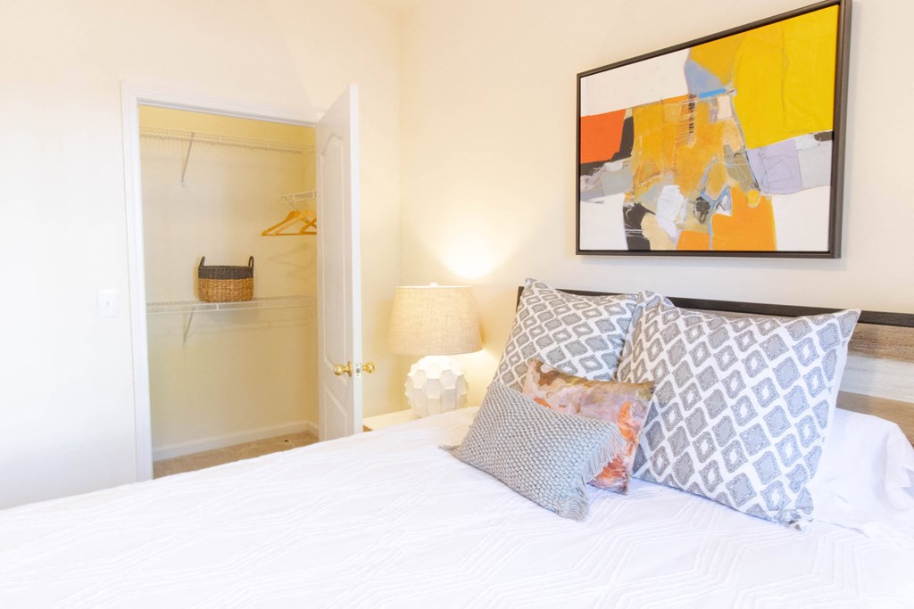 A bedroom with a bed, pillows, a painting, and a closet. at The Crest at Sugarloaf, Lawrenceville, 30044