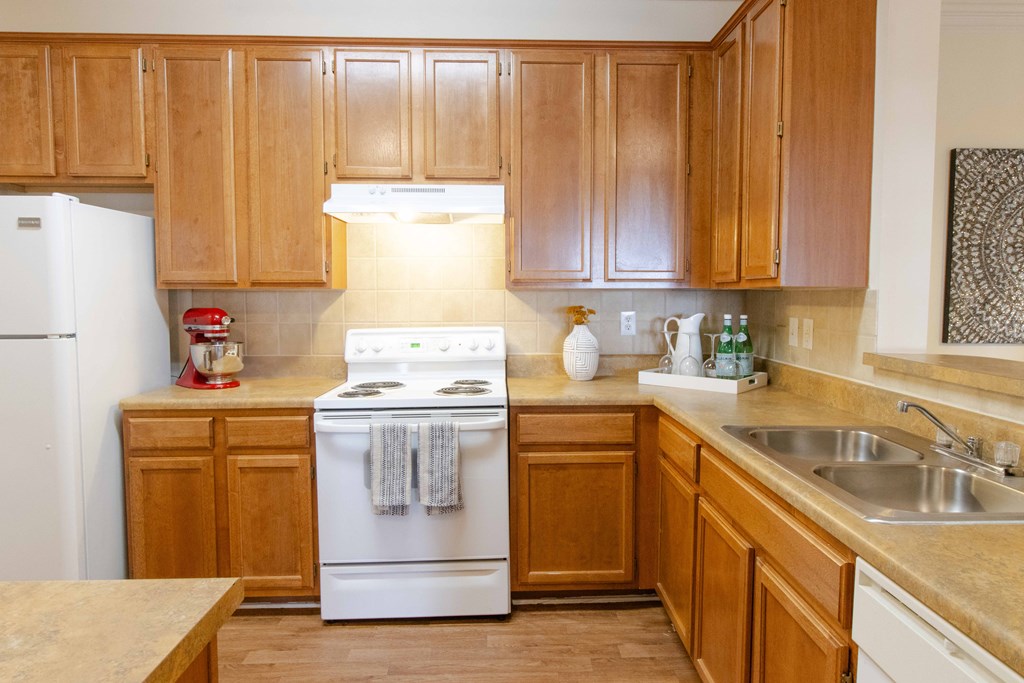 A kitchen with wooden cabinets and a white stove top oven at The Crest at Sugarloaf Apartments, Lawrenceville