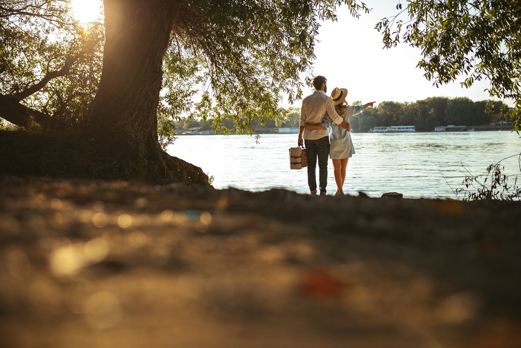 a man and a woman standing under a tree by the water at District at Riverside Apartments, Chattanooga