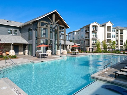 A large swimming pool in front of a building with a patio and umbrellas.
