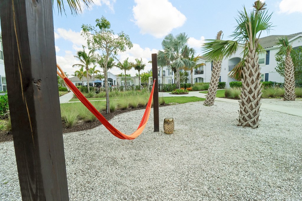 a red hammock in a gravel area with palm trees and houses in the background at The Crest at Naples, Florida, 34113
