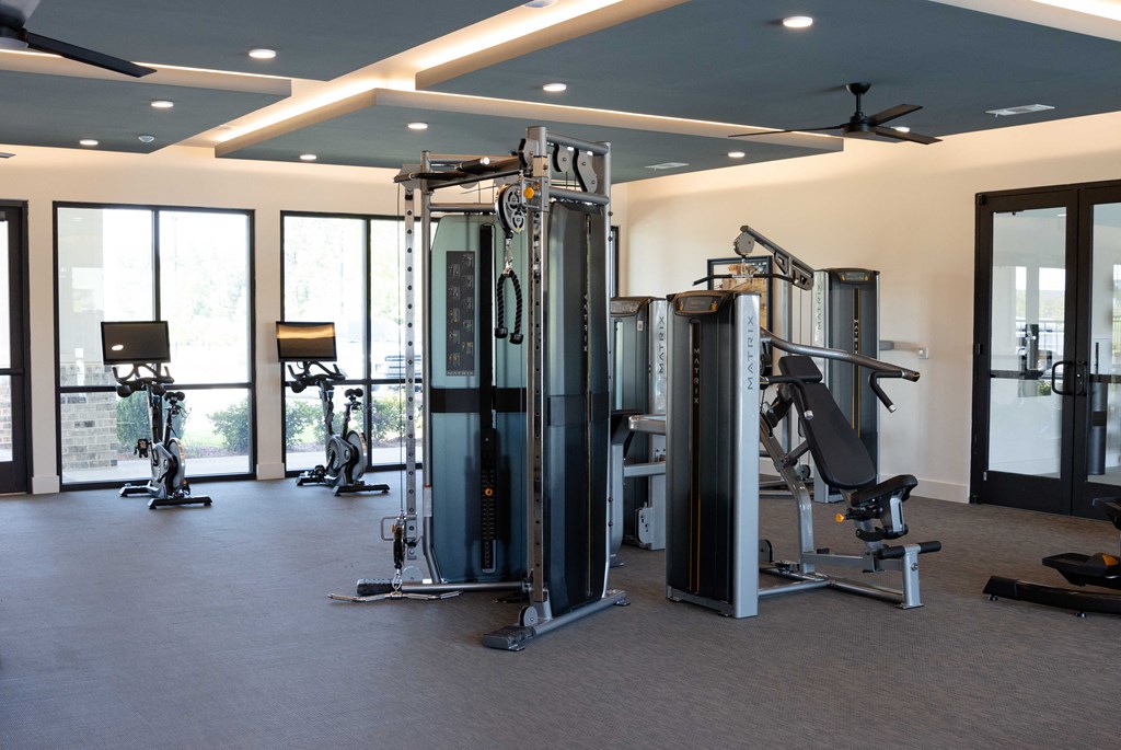 A gym with a variety of equipment including a squat rack, a leg press machine, and a bench press. at The Crest at South Point Apartments, Davenport  30253