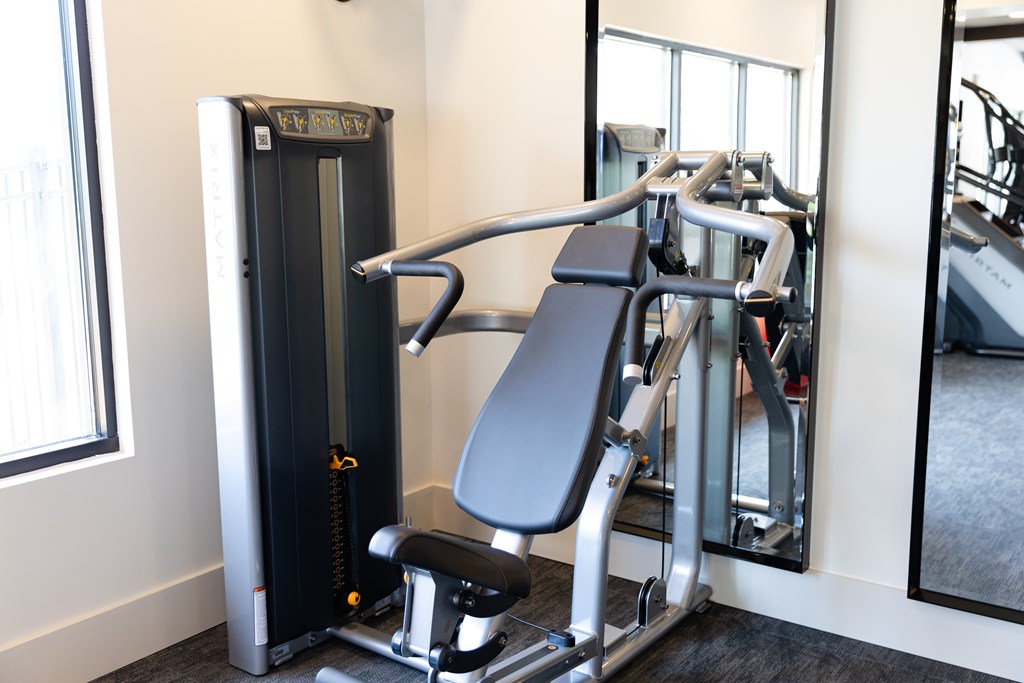 A gym with a weight machine and a mirror. at The Crest at Oakwood Apartments, Georgia