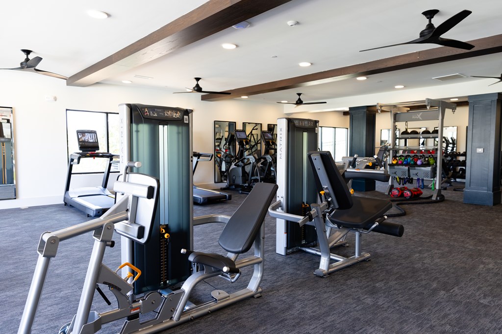 A gym with a variety of equipment including treadmills, weight machines, and a bench press. at The Crest at Oakwood Apartments, Oakwood 