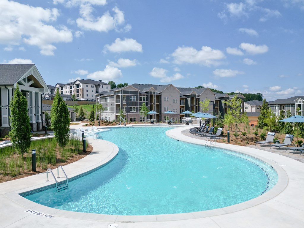 A large outdoor swimming pool surrounded by lounge chairs and umbrellas. at The Crest at Oakwood Apartments, Georgia