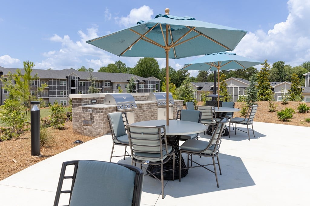 A patio with a table and chairs under an umbrella. at The Crest at Oakwood Apartments, Oakwood , GA