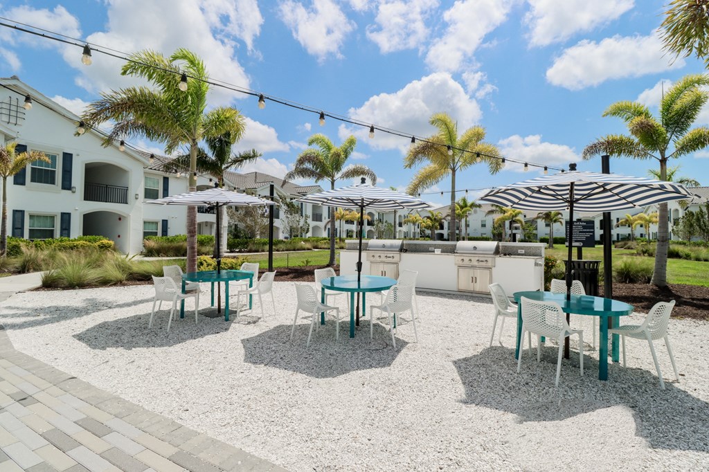Community grilling stations with umbrella covered table with chairs  at The Crest at Naples, Naples, FL