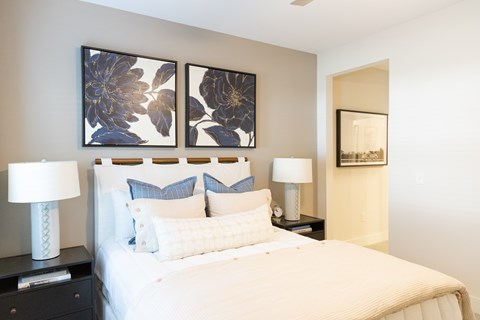 Primary bedroom with a staged bed, bedside tables and framed artwork in a two-bedroom model apartment at The Crest at Oakwood in Oakwood, GA.