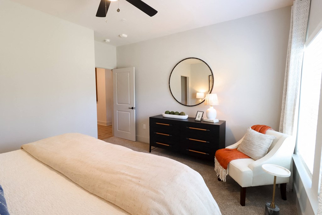 a bedroom with a large bed and a chair and a dresser with a mirror at The Crest at South Point Apartments, Davenport  30253